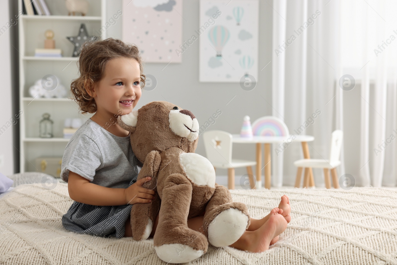 Photo of Cute little girl with teddy bear on bed at home