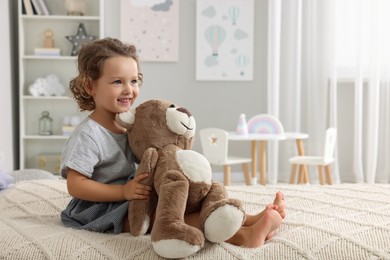 Cute little girl with teddy bear on bed at home