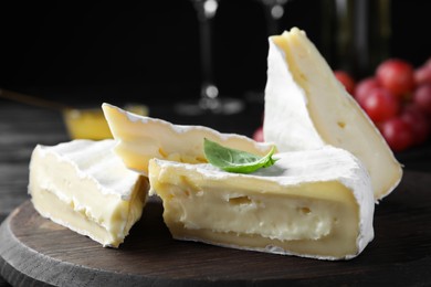 Photo of Tasty brie cheese with basil on wooden board, closeup