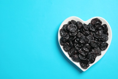 Photo of Heart shaped plate of sweet dried plums on color background, top view with space for text. Healthy fruit