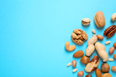 Different delicious nuts on light blue background, flat lay. Space for text