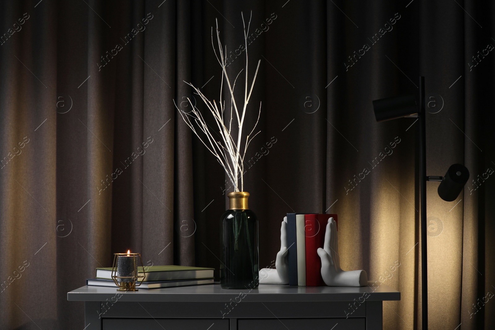 Photo of Vase with white tree twigs, books and candle on chest of drawers indoors
