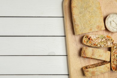 Photo of Tasty strudel with chicken, vegetables and sauce on white wooden table, top view. Space for text