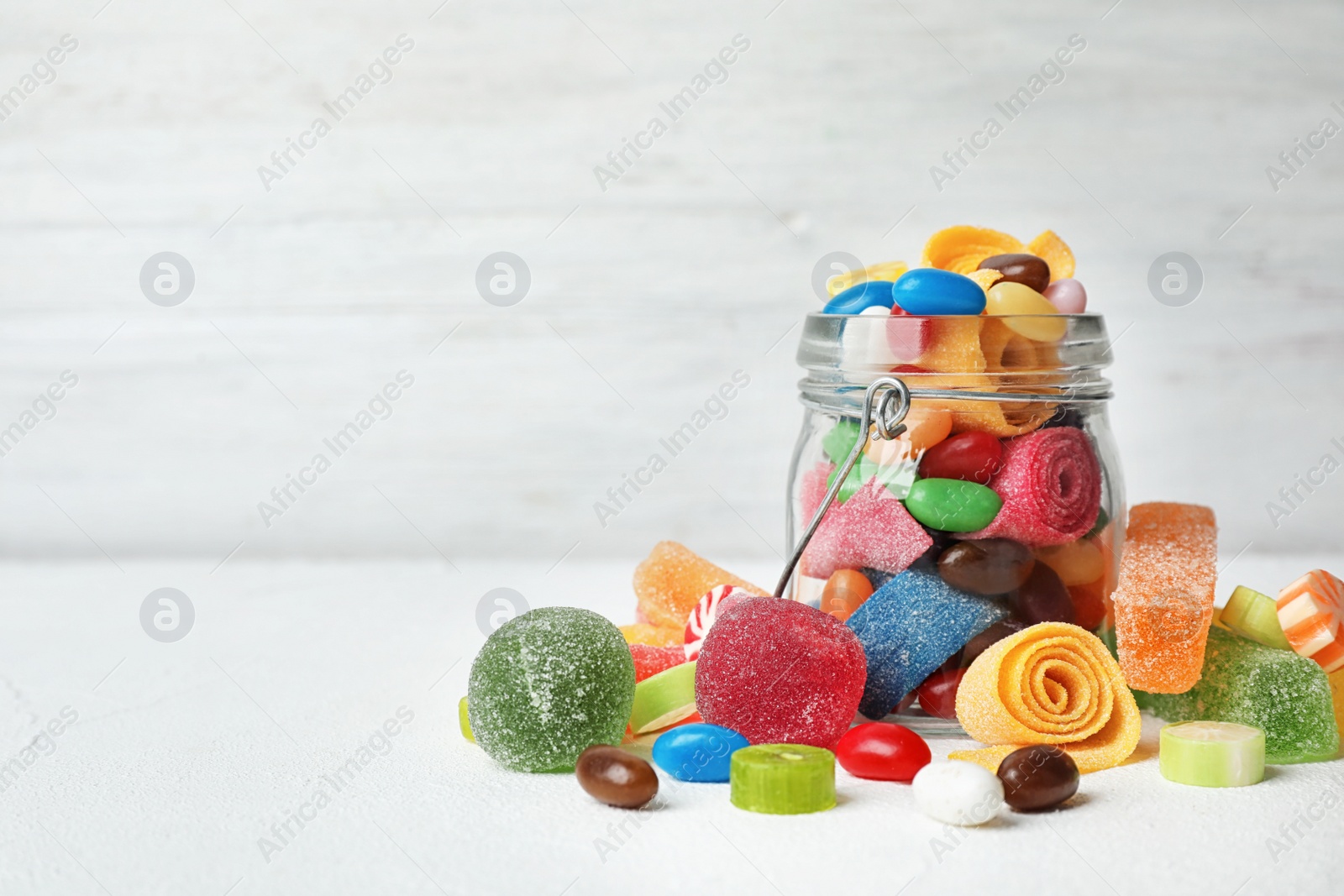 Photo of Jar with delicious colorful candies on table against light background. Space for text