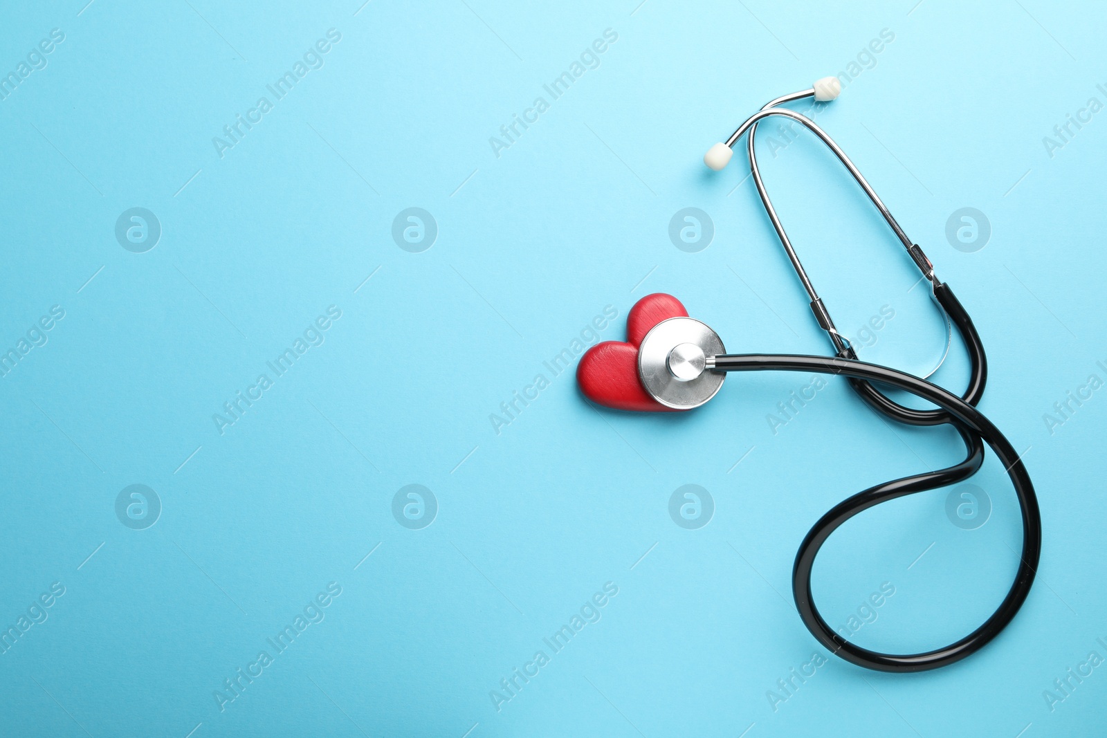 Photo of Stethoscope and red heart on light blue background, top view. Space for text