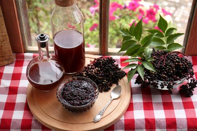 Elderberry drink and jam with Sambucus berries on table near window