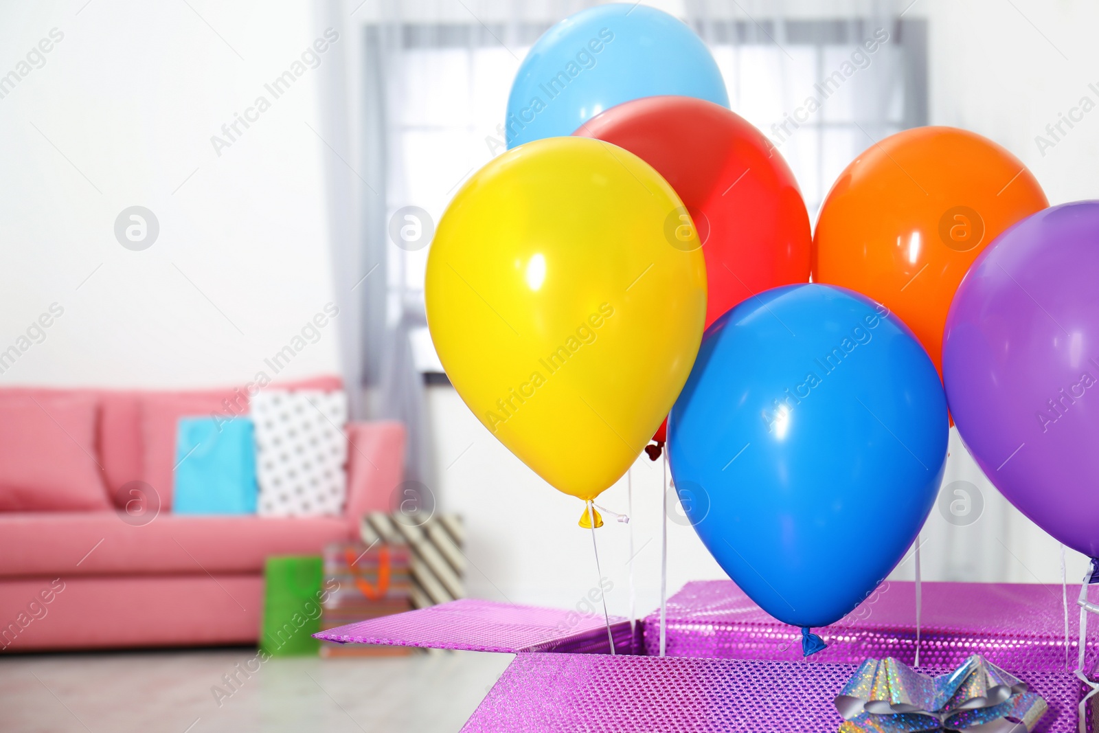 Photo of Gift box with bright air balloons in living room. Space for text