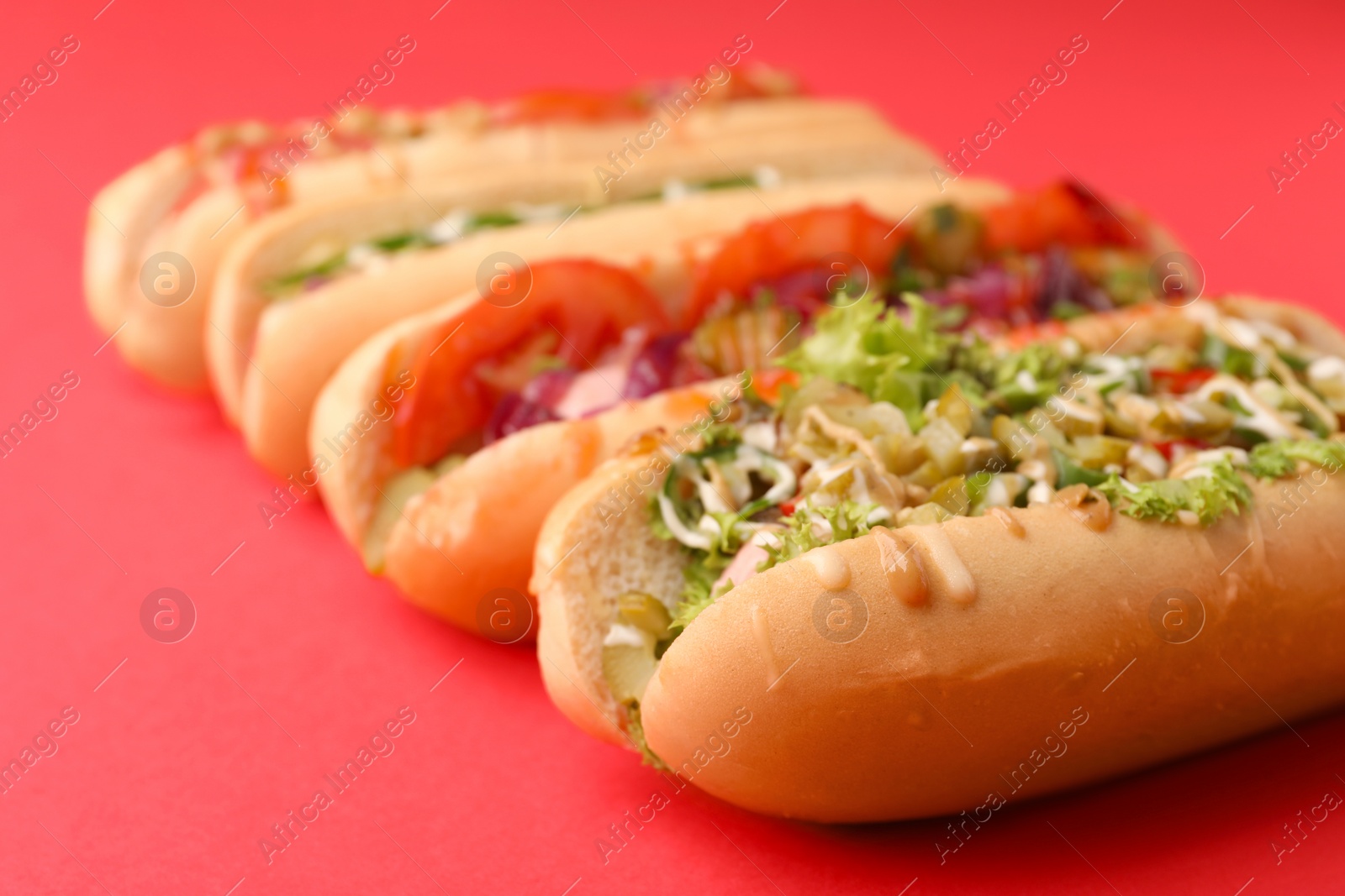 Photo of Delicious hot dogs with different toppings on red background, closeup