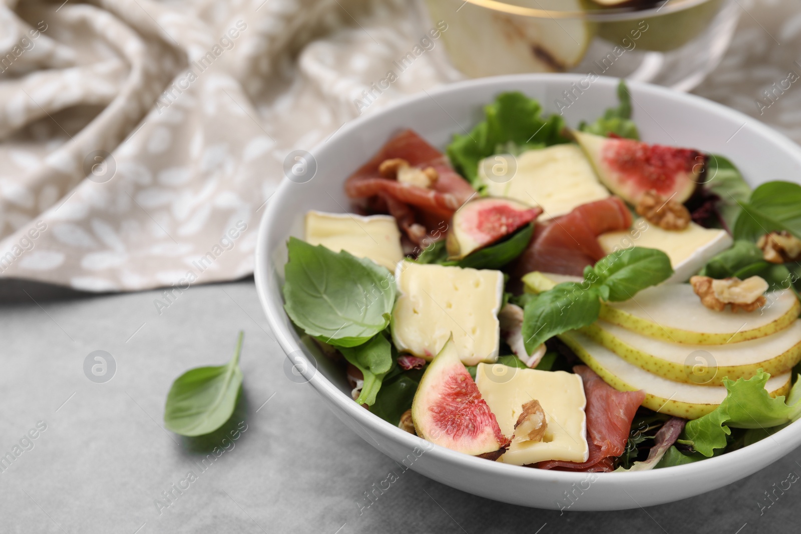 Photo of Tasty salad with brie cheese, prosciutto, pear and figs on grey table, closeup. Space for text