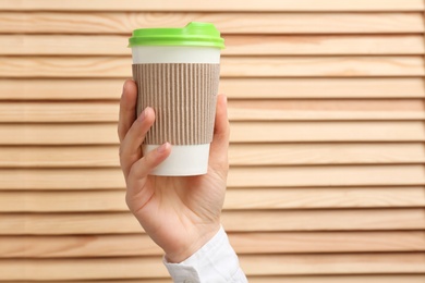 Photo of Woman holding takeaway paper coffee cup on wooden background. Space for text