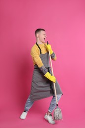 Photo of Handsome young man with mop singing on pink background
