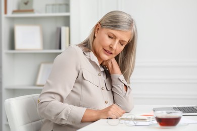 Photo of Woman suffering from neck pain at workplace in room