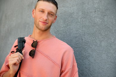 Photo of Handsome young man with stylish sunglasses and backpack near grey wall, space for text