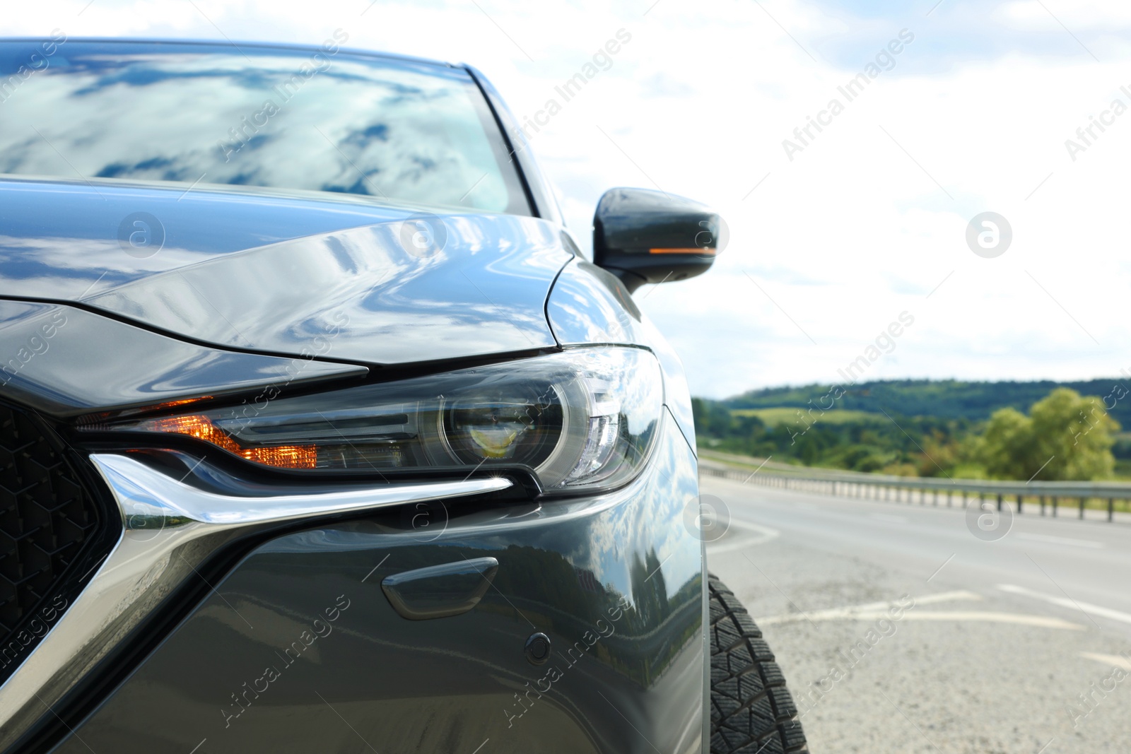 Photo of New black modern car on asphalt road, closeup of headlight