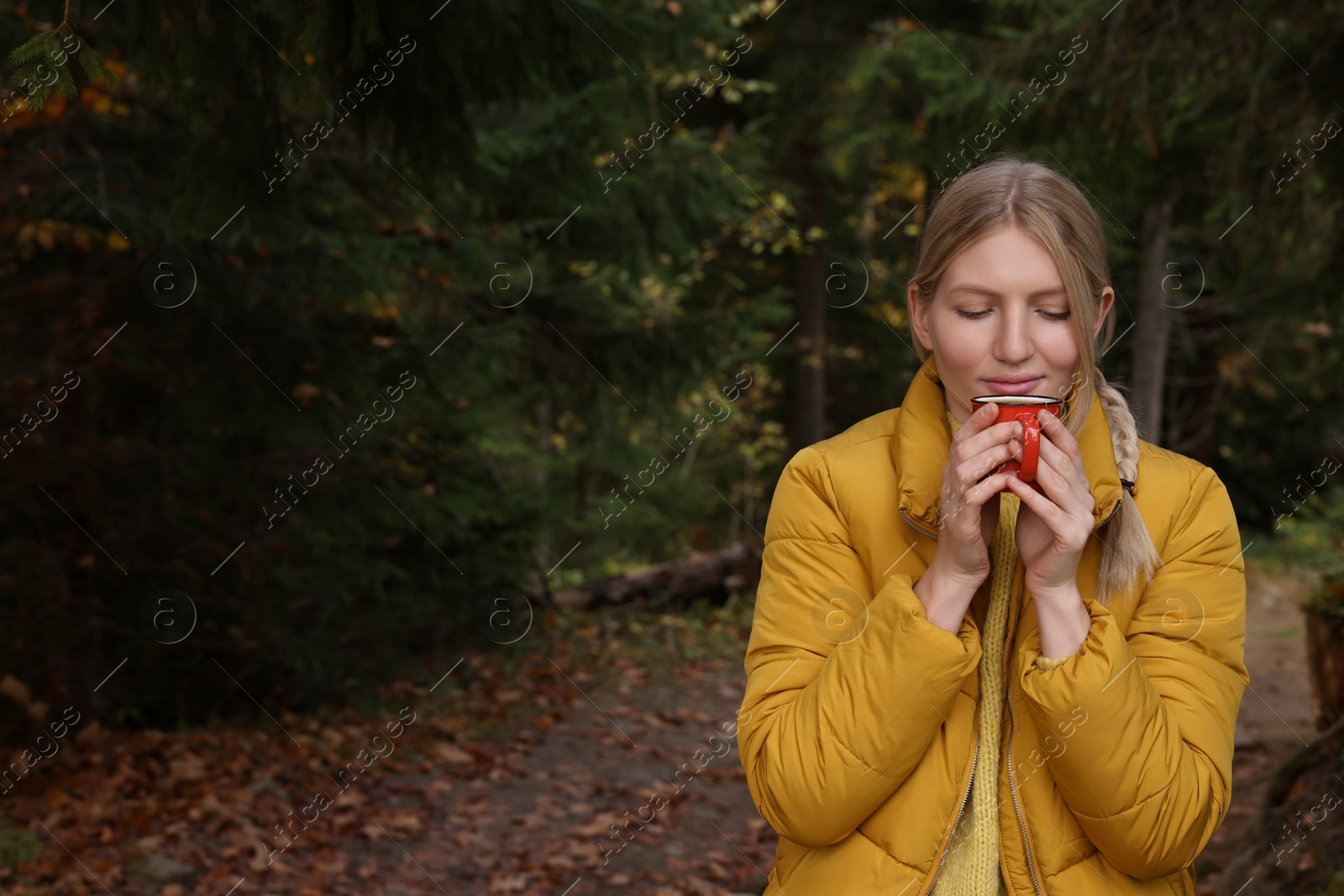 Photo of Young woman with mug of hot instant coffee near forest in autumn