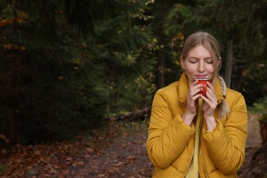 Photo of Young woman with mug of hot instant coffee near forest in autumn