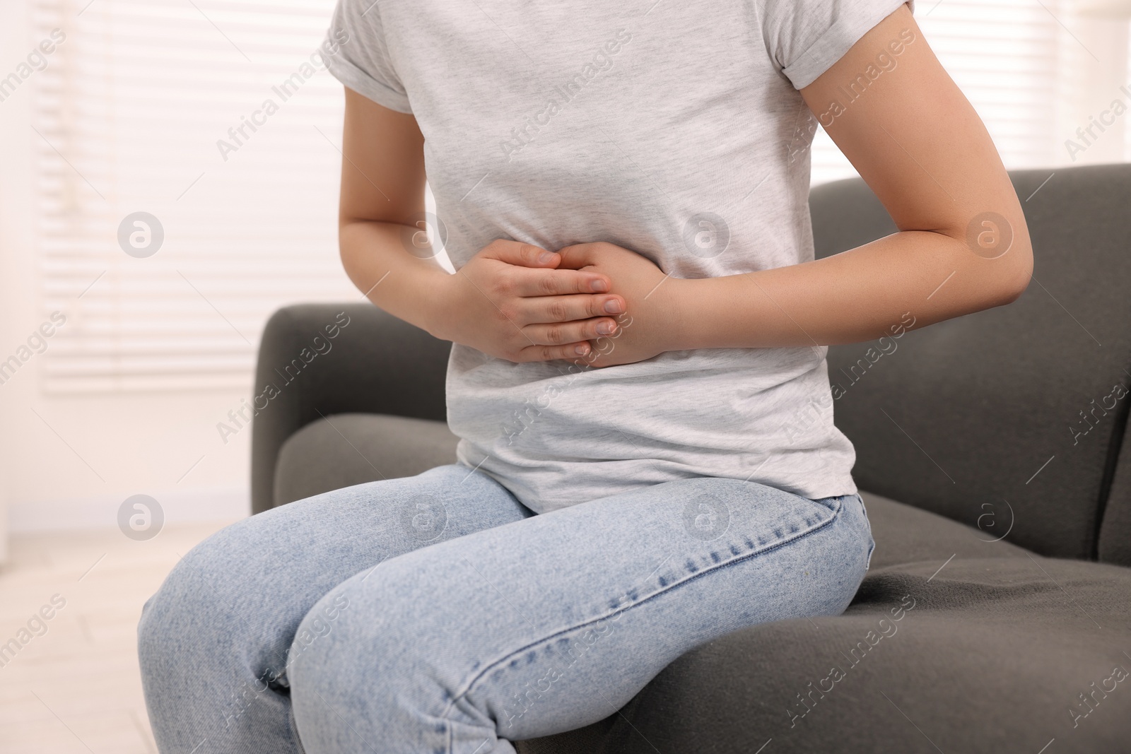 Photo of Woman suffering from abdominal pain indoors, closeup. Unhealthy stomach