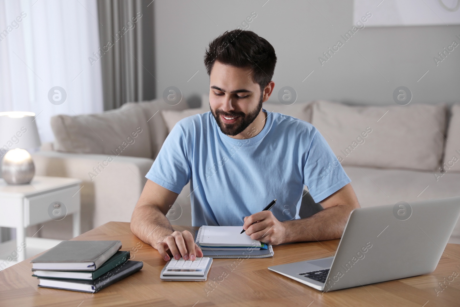 Photo of Young man counting on calculator during webinar at table in room