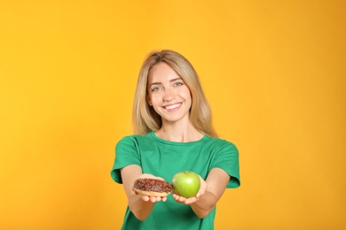 Photo of Woman choosing between doughnut and healthy apple on yellow background