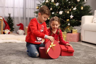 Photo of Cute little children with gift boxes near Christmas tree at home