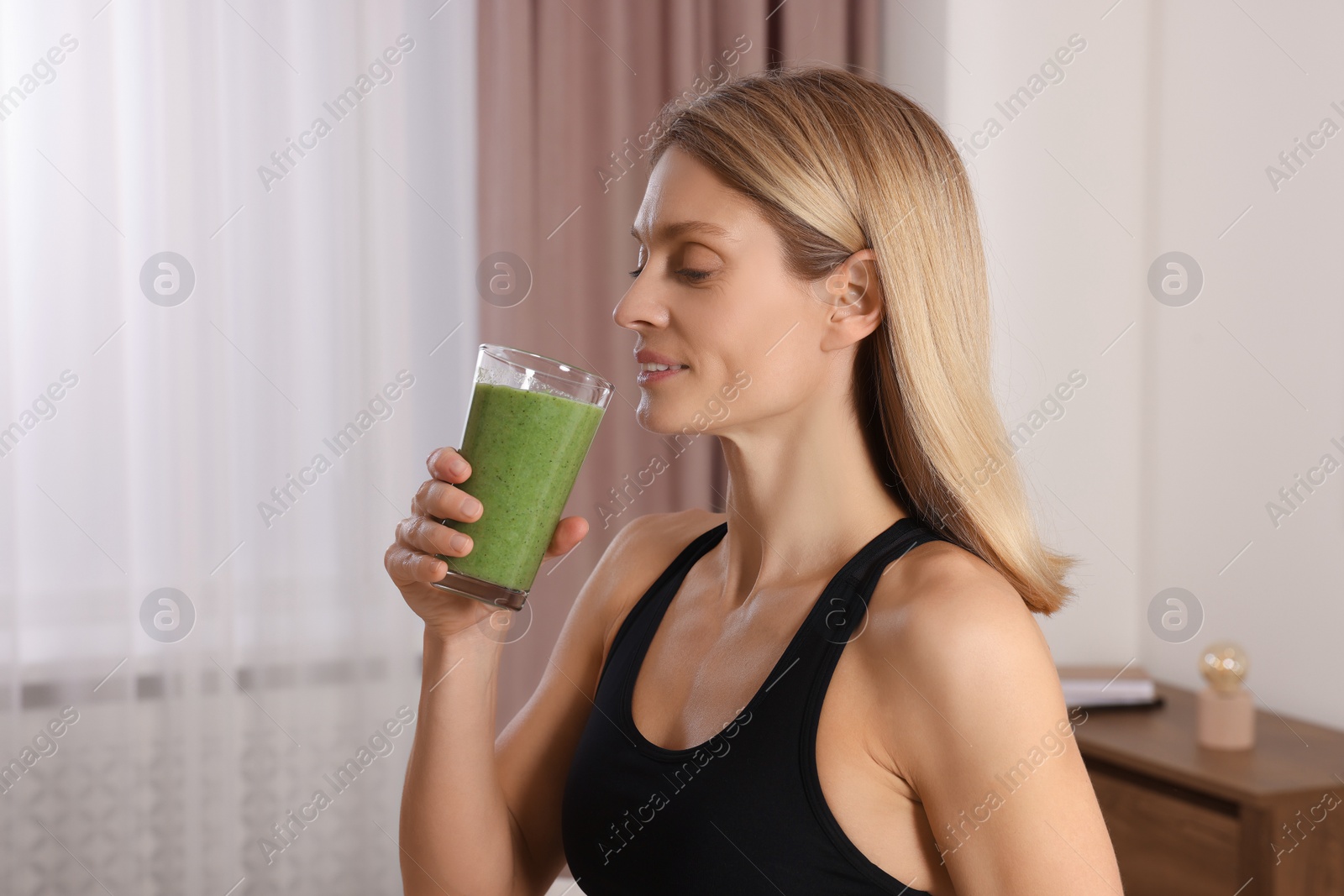 Photo of Young woman in sportswear with glass of fresh smoothie at home