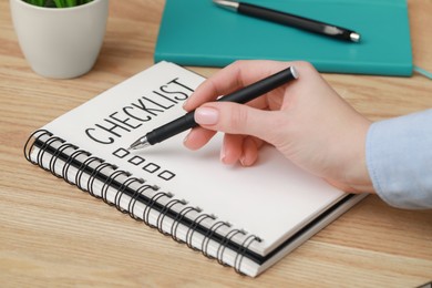 Photo of Woman filling Checklist with pen at wooden table, closeup