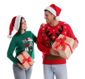 Photo of Beautiful happy couple in Santa hats and sweaters holding Christmas gifts on white background