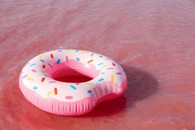 Photo of Bright inflatable ring floating in pink lake on summer day