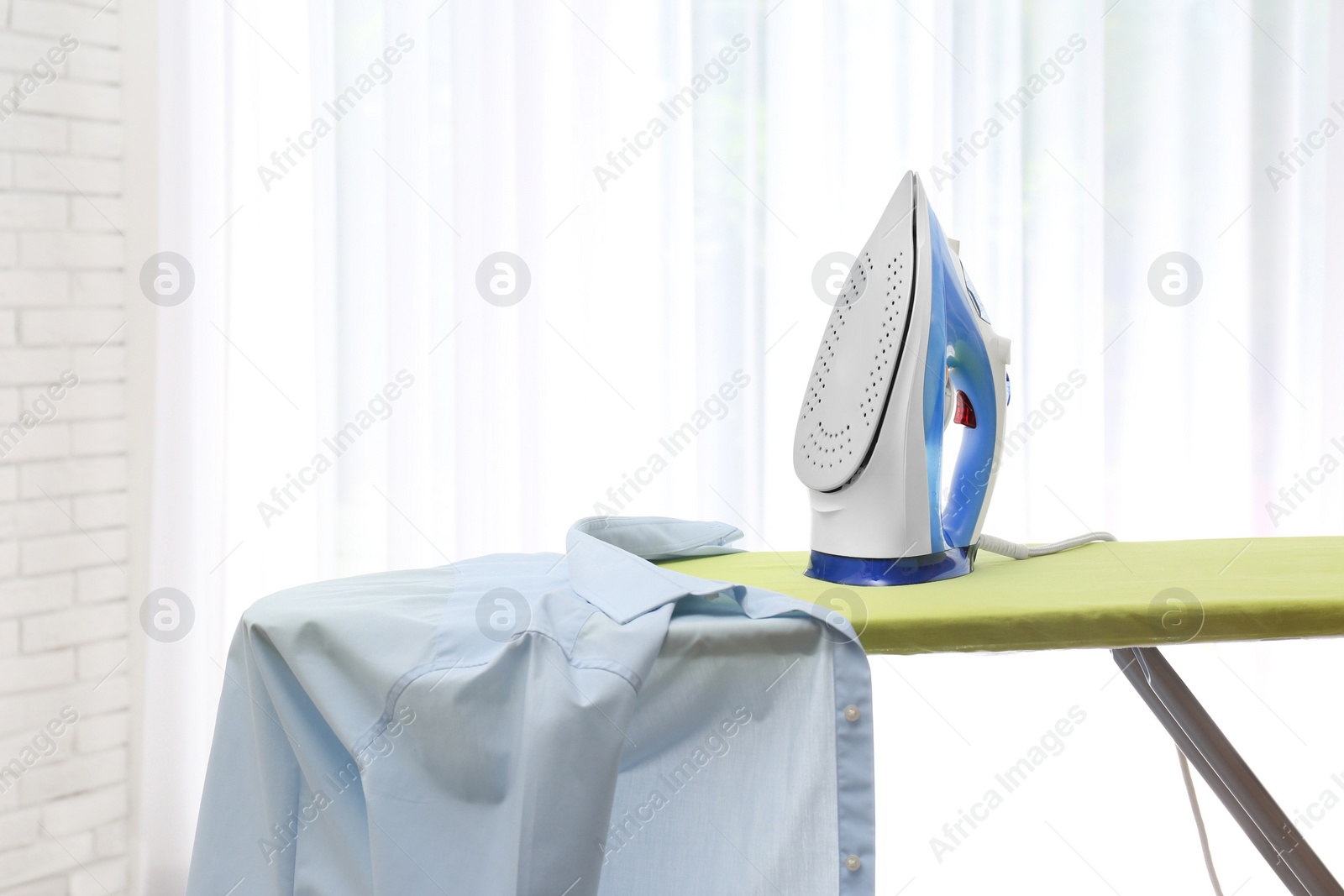 Photo of Board with modern iron and shirt at home. Laundry day