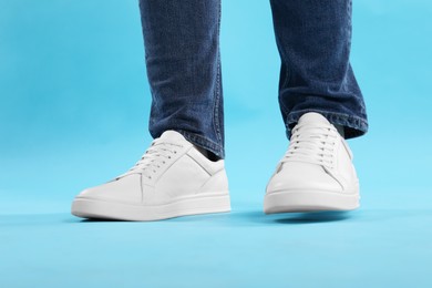 Photo of Man wearing stylish white sneakers on light blue background, closeup