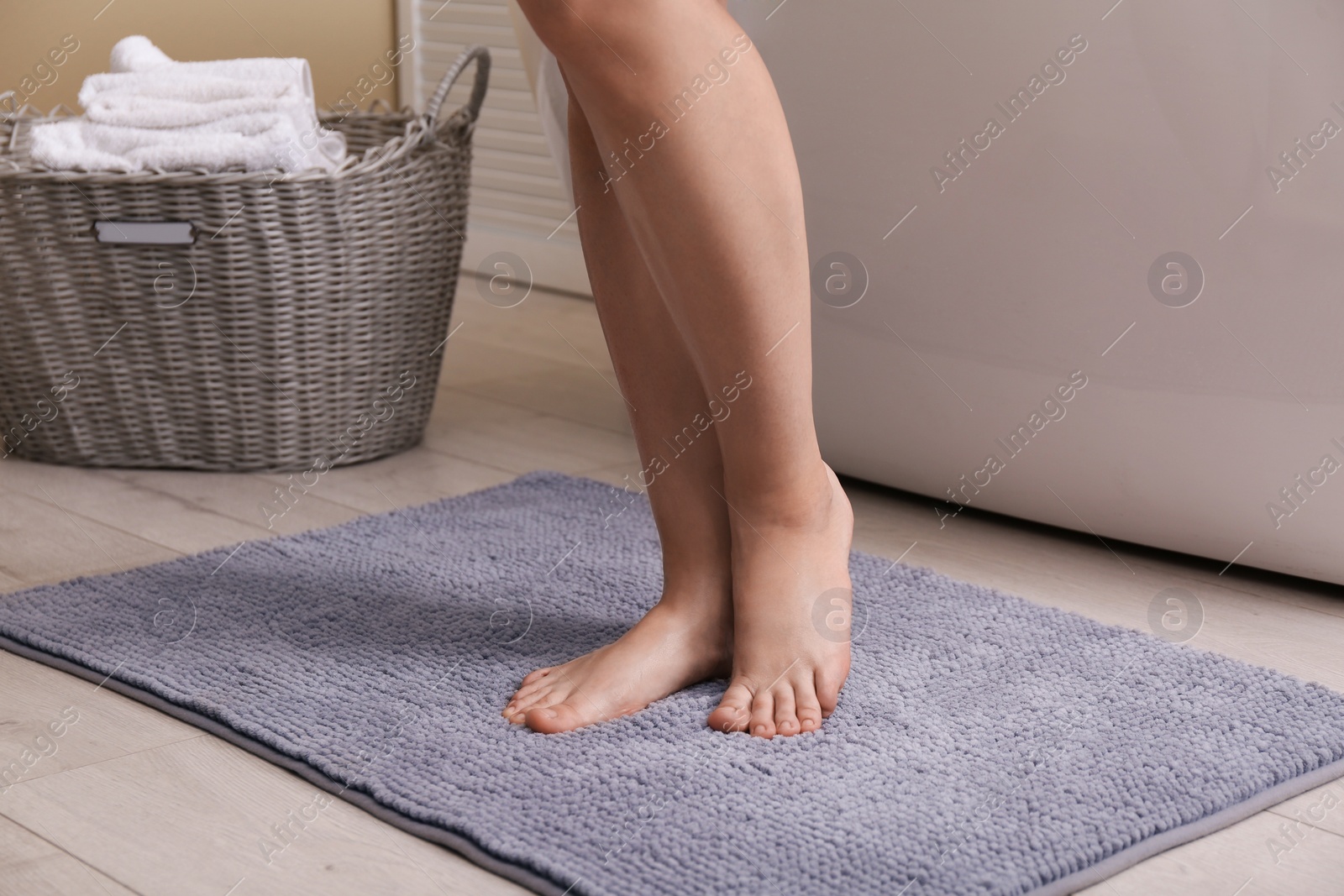Photo of Woman standing on soft grey bath mat near tub at home, closeup