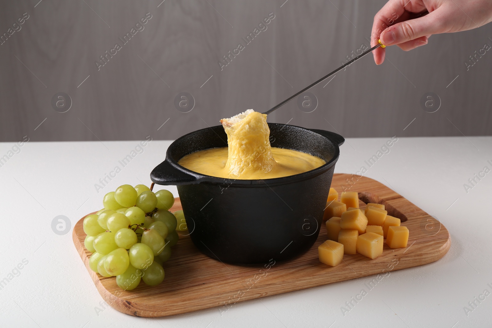 Photo of Woman dipping piece of bread into fondue pot with tasty melted cheese at white table, closeup