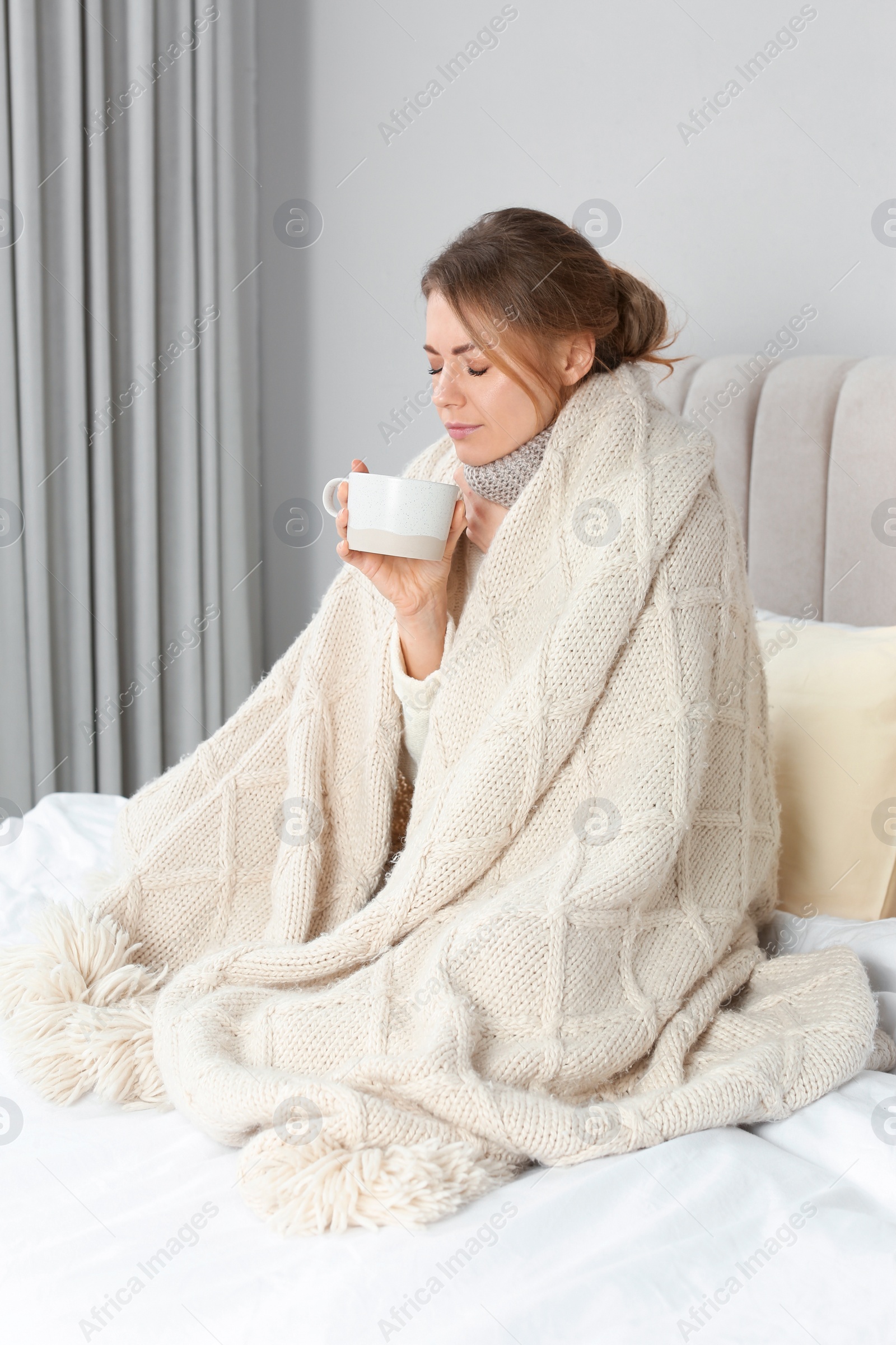 Photo of Sick woman with warm plaid and cup of drink in bed at home