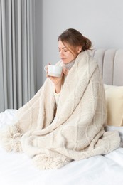 Photo of Sick woman with warm plaid and cup of drink in bed at home