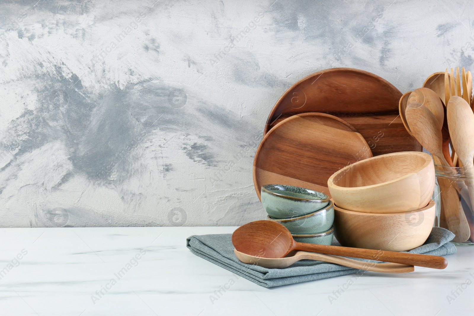 Photo of Different dishware and utensils on white marble table against textured wall. Space for text