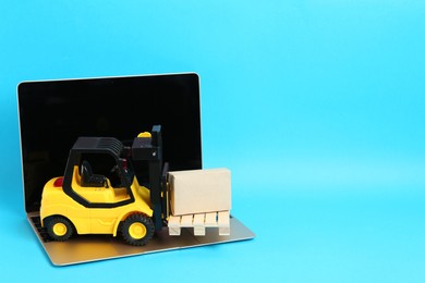 Photo of Laptop, toy forklift with wooden pallet and box on light blue background, space for text