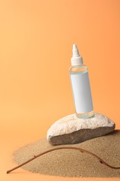 Photo of Bottle with serum, branch and stone on sand against orange background, space for text. Cosmetic product