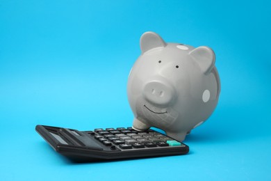 Piggy bank and calculator on light blue background