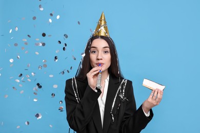Photo of Woman in party hat with blower, piece of tasty cake and flying confetti on light blue background