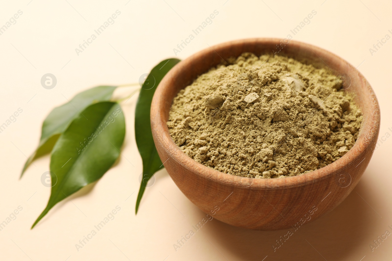 Photo of Henna powder and green leaves on beige background, closeup. Natural hair coloring