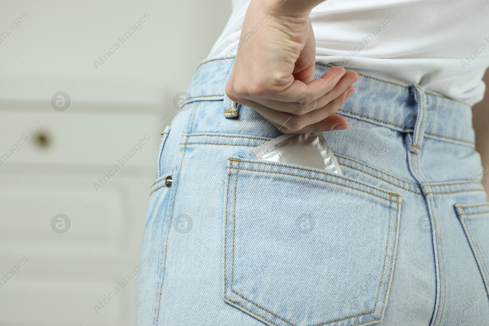 Photo of Woman pulling condom out of pocket indoors, closeup. Safe sex