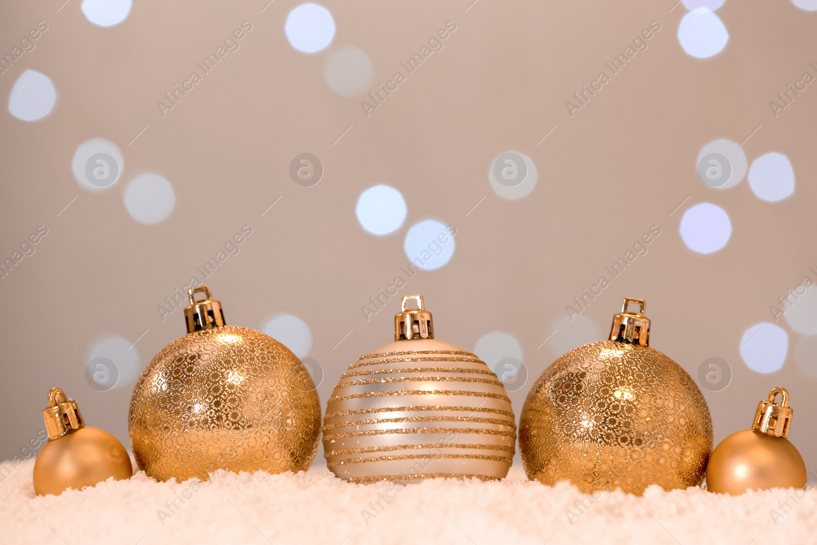 Photo of Beautiful golden Christmas balls on snow against blurred festive lights. Space for text