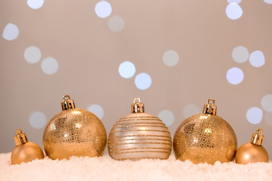 Photo of Beautiful golden Christmas balls on snow against blurred festive lights. Space for text