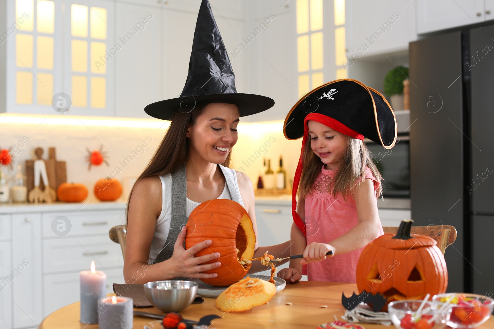 Photo of Mother and daughter making pumpkin jack o'lantern at table in kitchen. Halloween celebration