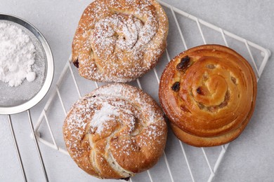 Different delicious rolls with sugar powder on light grey table, flat lay. Sweet buns