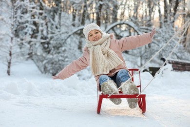 Cute little girl enjoying sledge ride through snow in winter park