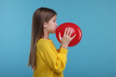Cute girl inflating red balloon on light blue background