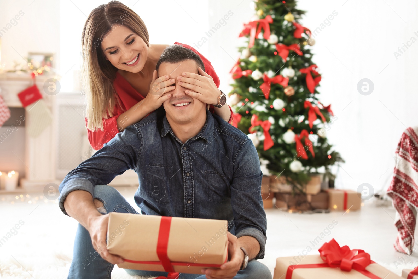 Photo of Young woman surprising her boyfriend with Christmas gift at home