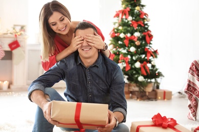 Young woman surprising her boyfriend with Christmas gift at home