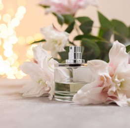 Bottle of perfume and beautiful lily flowers on table against beige background with blurred lights, closeup